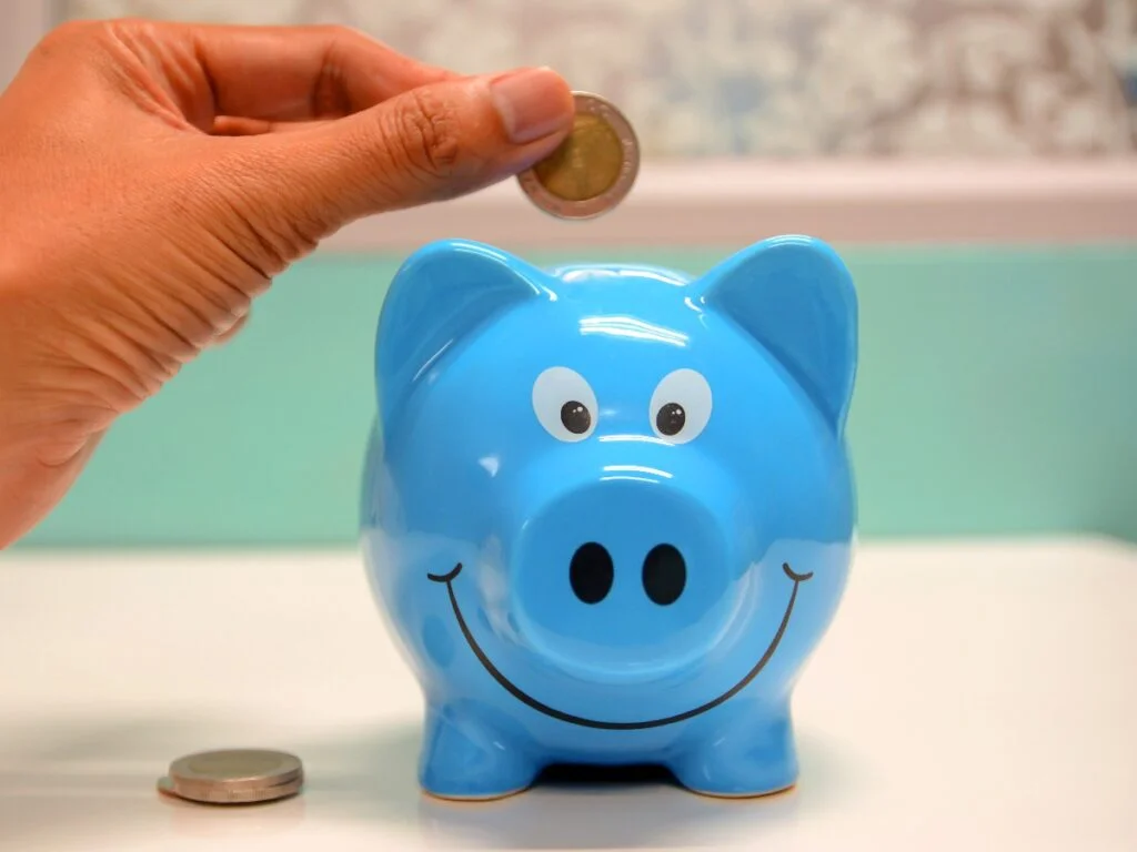Person putting money into blue piggy bank
