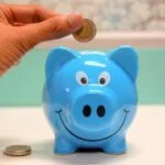 Person putting money into blue piggy bank