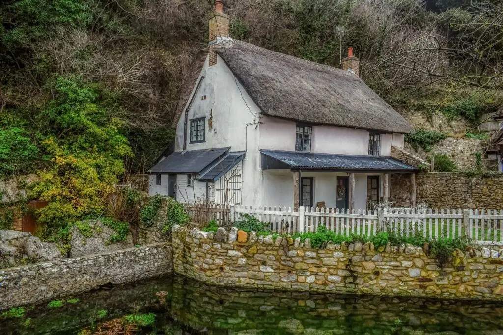 A quaint cottage with a thatched roof nestled next to a serene pond.