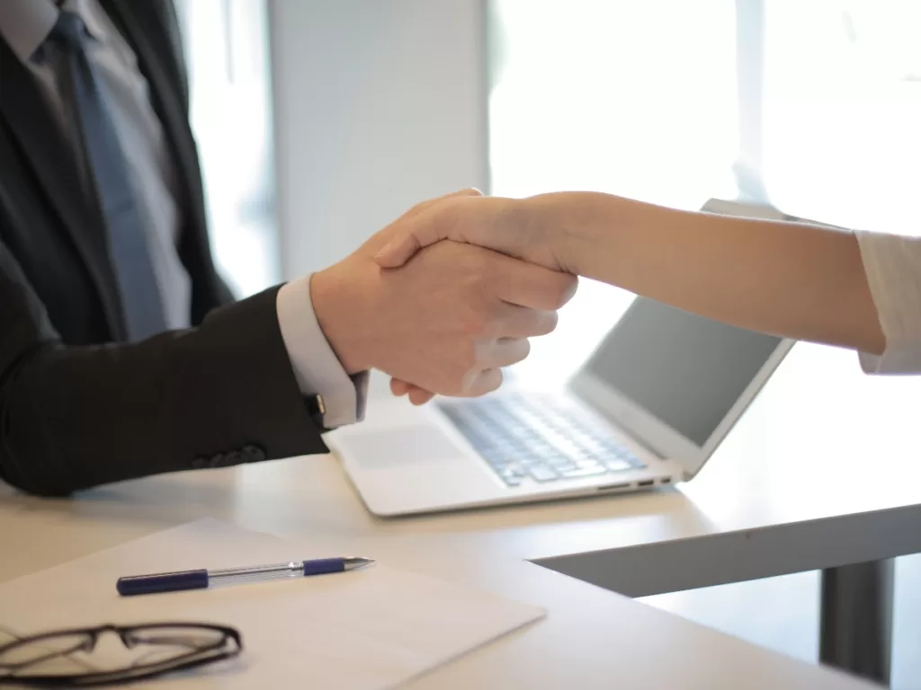 Handshake over desk with laptop