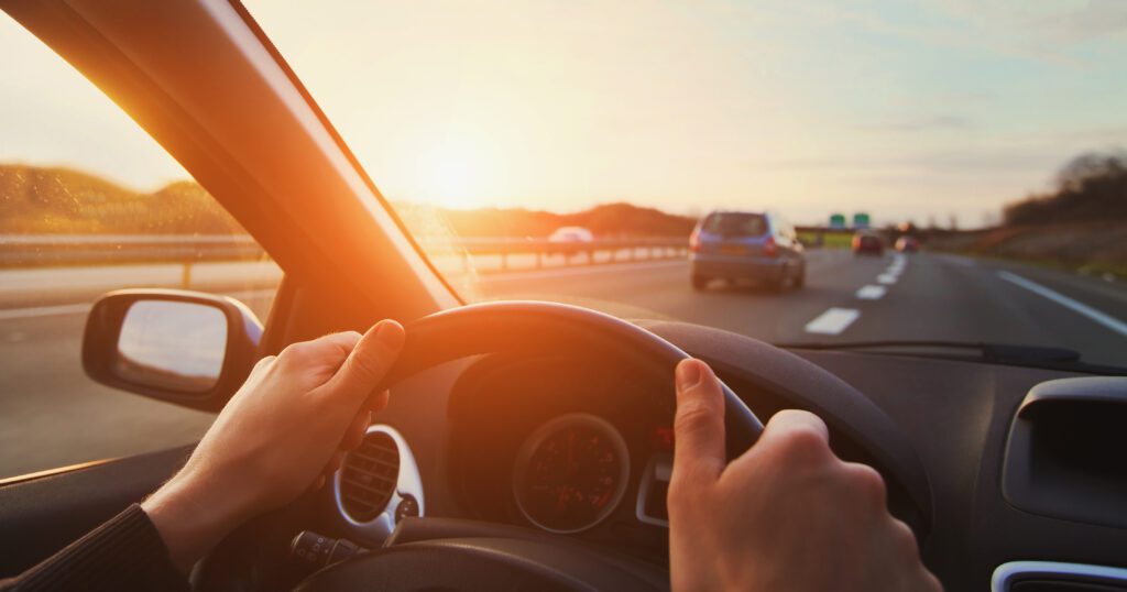 July 2026 Newsletter 3 hands of car driver on steering wheel, road trip, driving on highway road