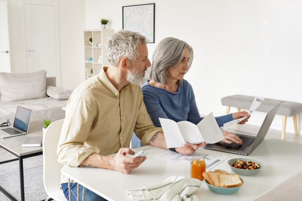 October 2026 Newsletter 3 Middle aged couple paying financial bills online using computer at home. Older mature husband and wife checking bank documents, reading papers, calculating taxes, planning retirement pension.