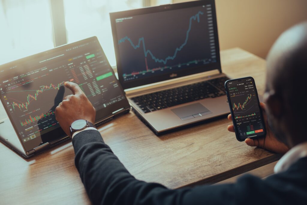 Young man holding a smartphone and laptop with online trading chart of crypto on the screen