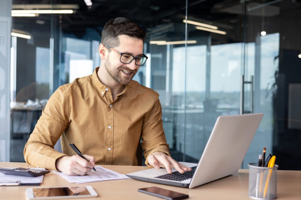 July 2026 Newsletter 5 Smiling male businessman sits in the office at the table, works with documents and talks with conducts a business meeting online.