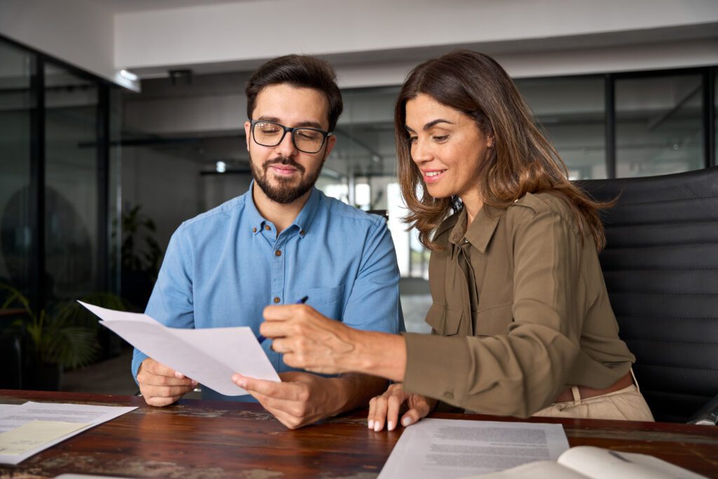 August 2026 Newsletter 3 Smiling female financial advisor, attorney lawyer or bank manager consulting client investor reading document at business meeting reviewing legal paper file planning taxes working in office.