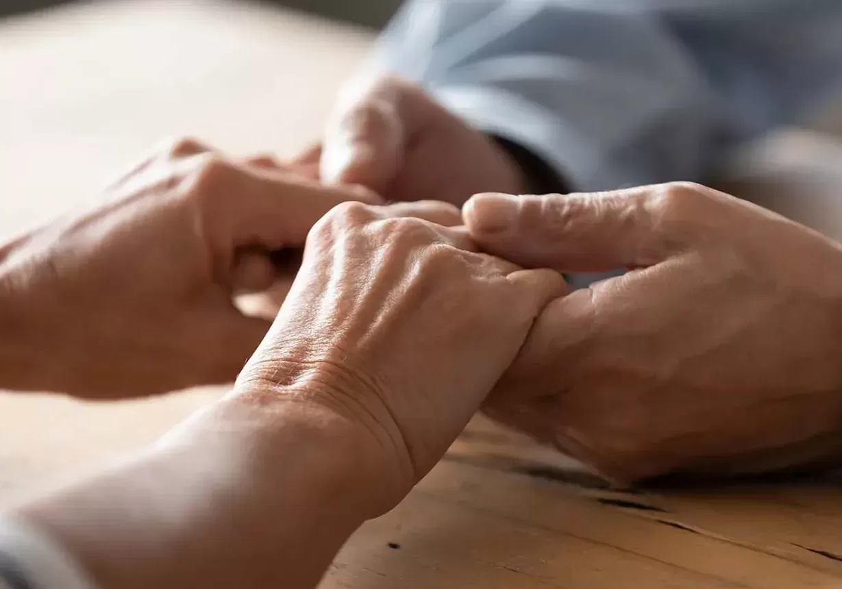 Two people, embodying trust and connection, gracefully hold hands on a sturdy wooden table.