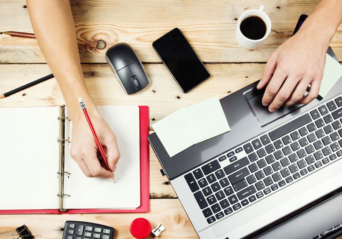 A person in the sectors working on a laptop with a pen and paper.